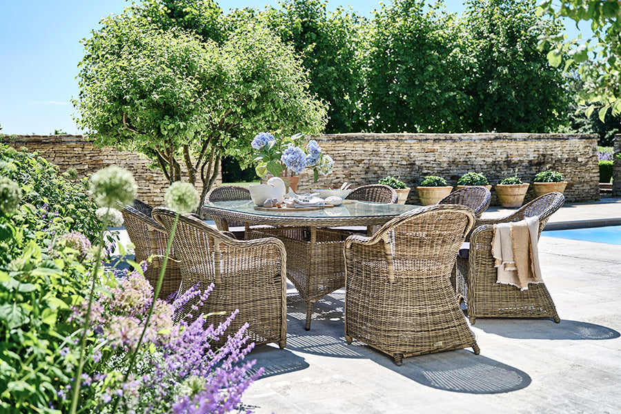Luxury rattan dining set, oval dining table with eight dining armchairs on a sunny patio.